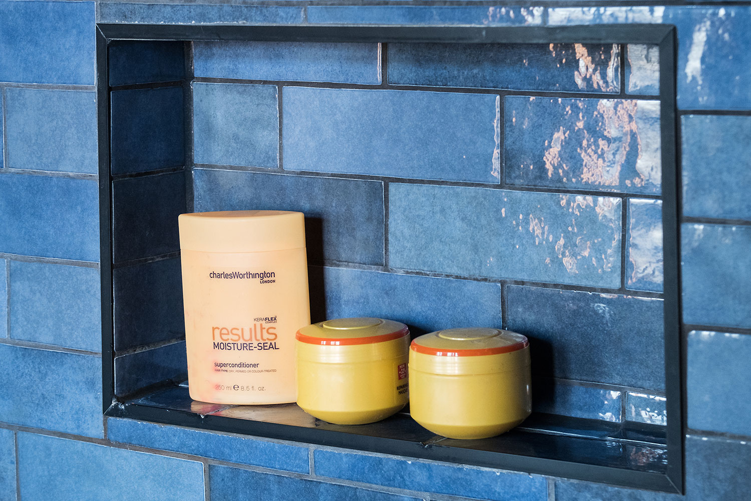 A blue tiled recess in a customer's bathroom with bottles of hair product.