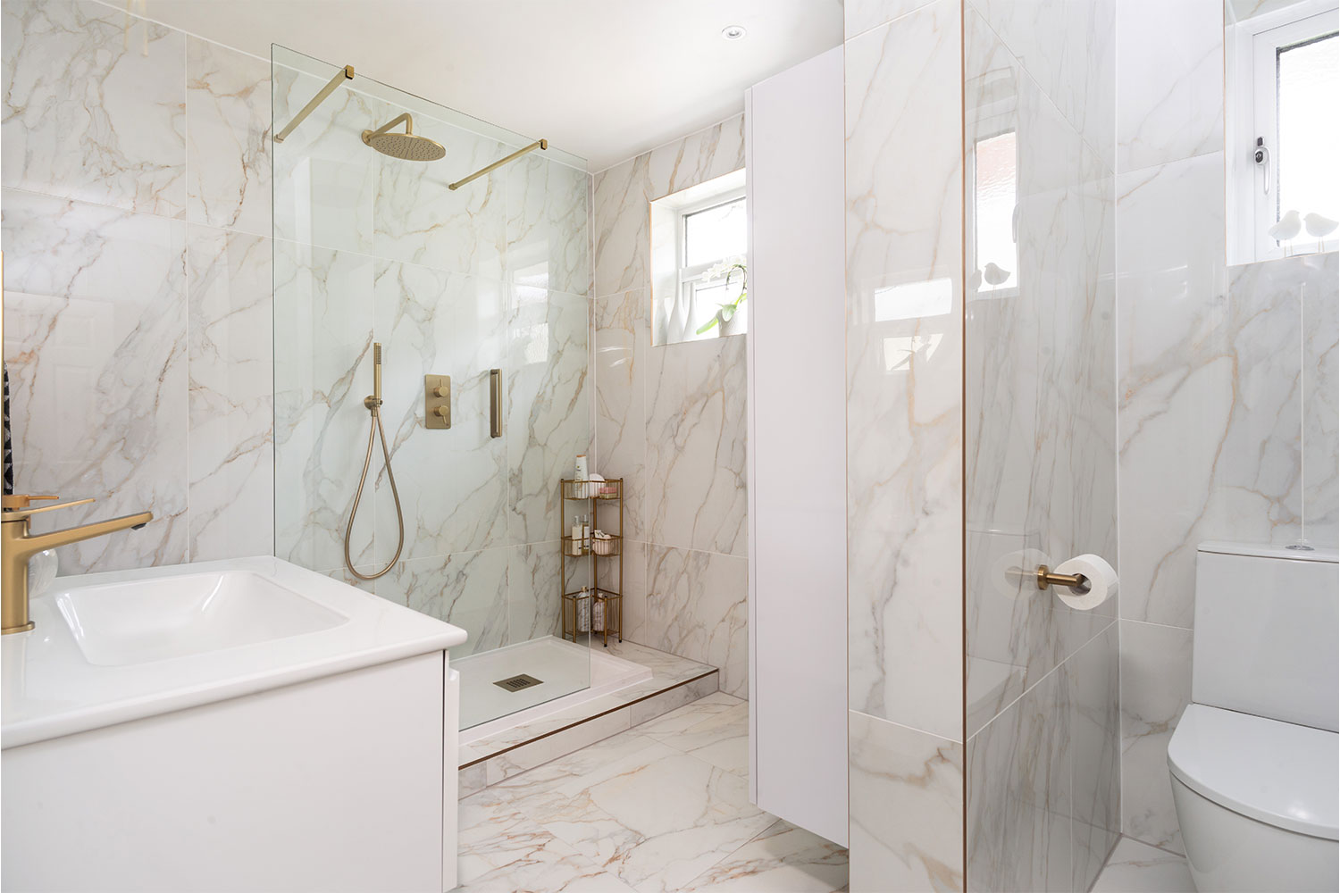 A bathroom with marble effect walls and floors, walk in shower and wc.