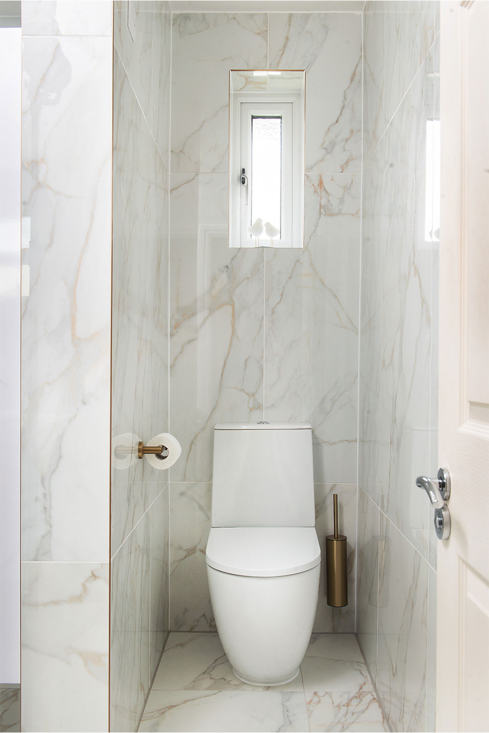 A white wc within a customers fully marble effect tiled bathroom.