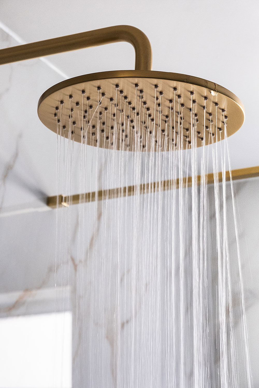 A brushed brass showerhead with running water.